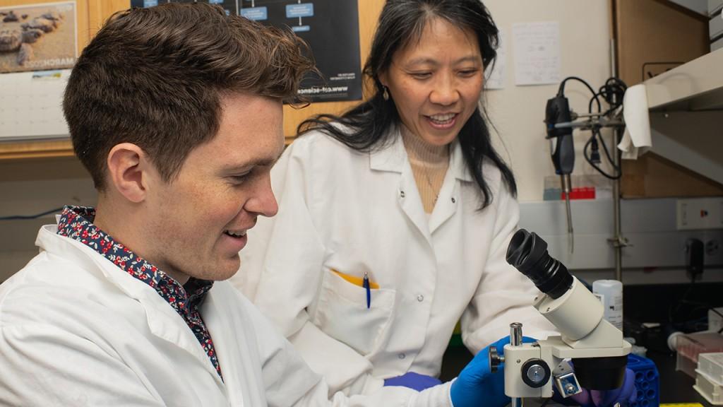 Ling Cao assists a student with a microscope