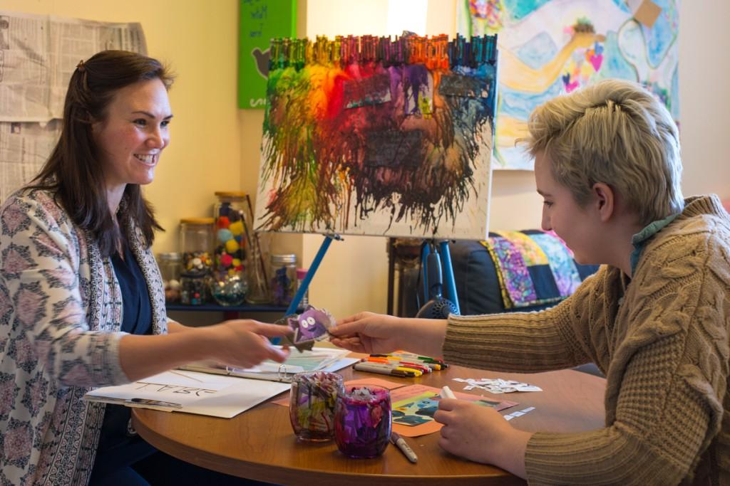 A social work student sits with a client as they paint