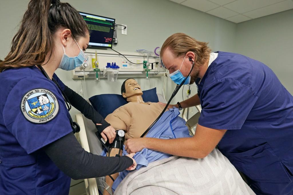 One A B S N student uses a stethoscope on a patient simulator as a fellow student watches