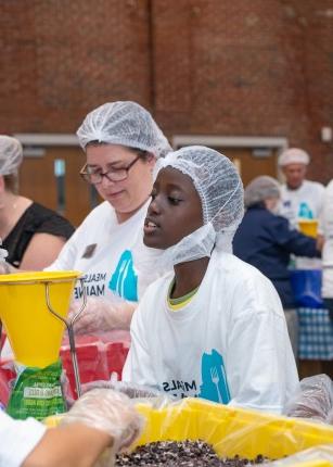 A young volunteer joins the crowd in packing meal kits