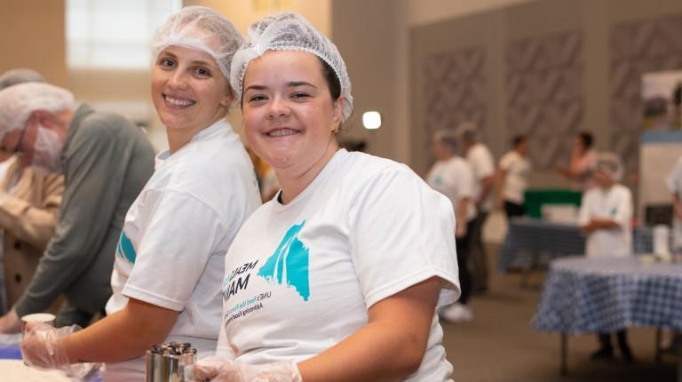 Two students pose for a photo while packing meals