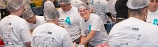 A volunteer smiles through the crowd of others helping to pack meal kits for the Meals for Maine event